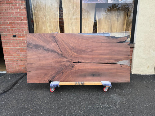 A Walnut wood dining table top with a smooth, polished surface featuring rich dark brown tones and distinctive grain patterns, complemented by a clear translucent epoxy resin fill that enhances the natural wood and creates a sleek, glossy finish.